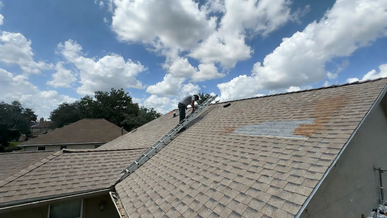 Texas roofing worker on ladder repairing hail damaged asphalt shingles on residential roof 2026